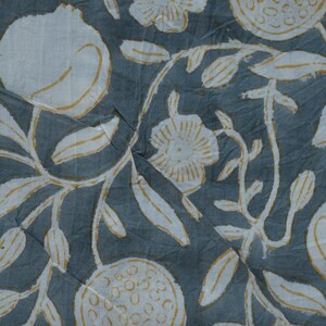 May include: Close-up of a fabric with a repeating pattern of white pomegranates, flowers, and leaves with yellow accents on a muted blue-gray background. The design has a hand-drawn, block-print style.