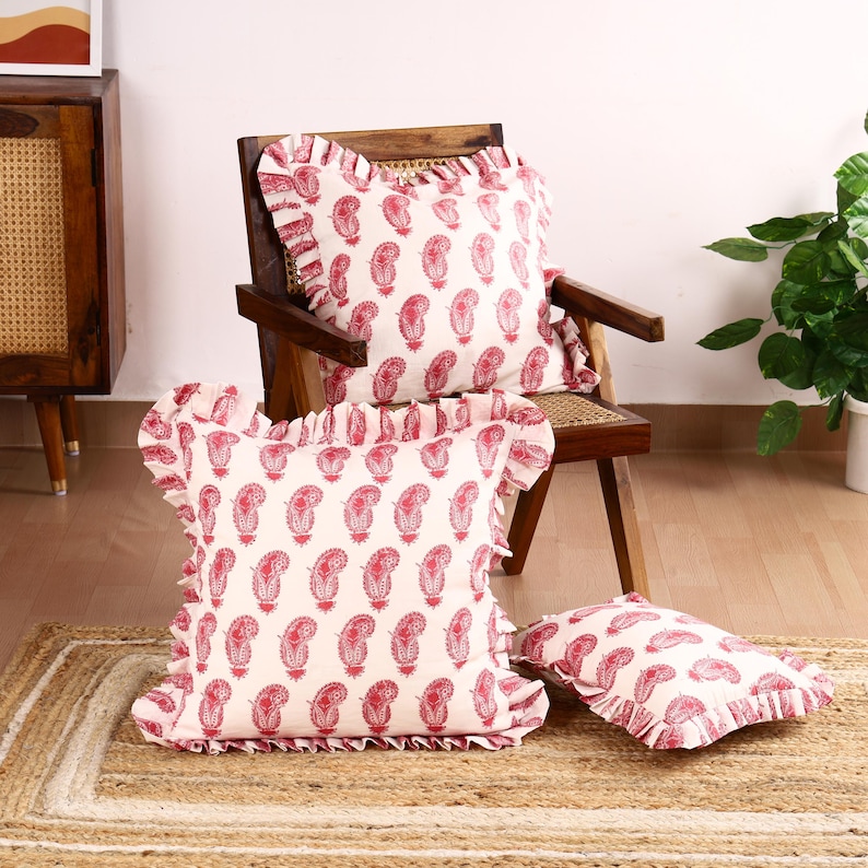 May include: Three white and pink patterned throw pillows with ruffled edges. The pillows are on a chair and a rug.