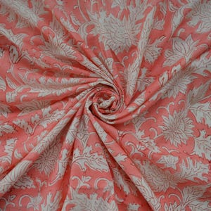 Könnte beinhalten: Ein rosa Baumwollstoff mit einem weißen Blumendruck. Der Stoff ist gefaltet und drapiert, wodurch Muster und Textur sichtbar werden.