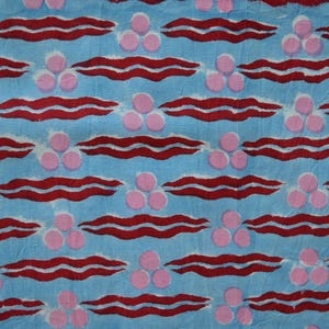 Könnte beinhalten: Hellblauer Stoff mit einem sich wiederholenden Muster aus roten, wellenförmigen Linien und Gruppen von drei rosa Kreisen. Das Design ist gleichmäßig verteilt und erzeugt eine strukturierte Optik. Ideal für Kleidung oder Heimtextilien.