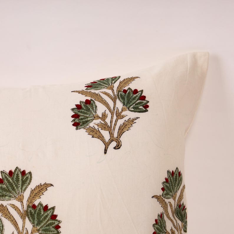 May include: Off-white pillow with a floral pattern. The design features green leaves, red flower buds, and tan stems. The pillow has a soft, textured appearance, suggesting a comfortable home decor item.