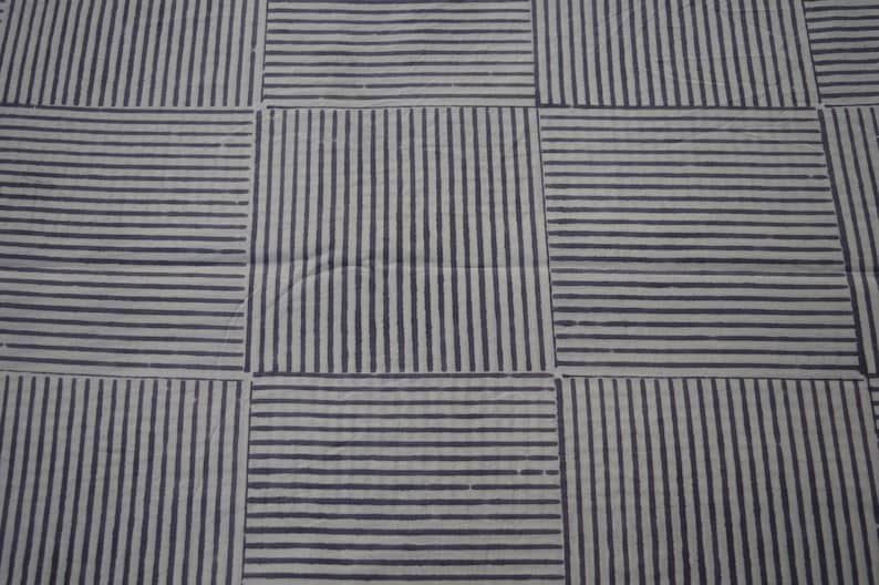 May include: A white fabric with a black striped pattern. The fabric is woven in a grid pattern with alternating horizontal and vertical stripes.
