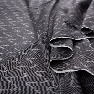 May include: Black fabric with a white geometric pattern. The fabric is folded and has a crinkled texture.