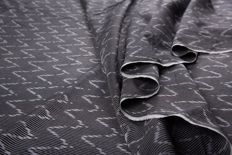 May include: Black fabric with a white geometric pattern. The fabric is folded and has a crinkled texture.