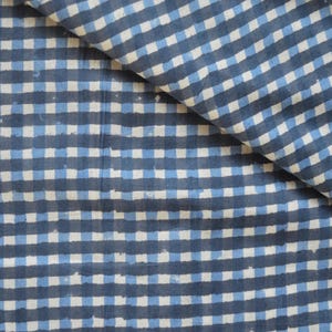 Puede incluir: Una tela textil que presenta un patrón de cuadrícula repetitivo de líneas horizontales y verticales en azul marino oscuro y azul claro sobre un fondo blanco. El diseño muestra una estética impresa a mano con bordes irregulares.