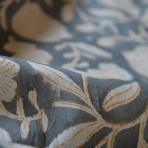 May include: Close-up of a fabric with a floral pattern. The fabric is a muted blue-gray color with white and yellow floral designs. The fabric is folded, showing the texture and detail of the print.