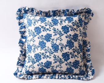 May include: Square throw pillow with a white background and a blue floral pattern. The pillow has a ruffled edge in a matching blue floral print. The pillow is a decorative home accent.