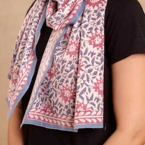 Può includere: Una sciarpa con motivo floreale rosa e blu su sfondo bianco. La sciarpa ha un bordo blu e un bordo rosa con un motivo bianco.