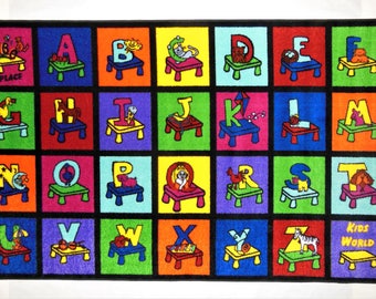 May include: A rectangular rug with a black border features colorful squares, each with a letter of the alphabet and a corresponding image. The rug has the text "MY PLACE" and "KIDS WORLD". The rug is designed for children.