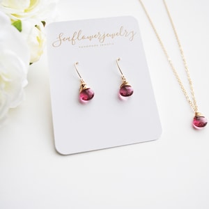May include: A set of pink gemstone jewelry featuring a necklace and earrings. The necklace and earrings have a gold wire wrapped around the pink gemstone. The card in the background says "Seaflowerjewelry handmade jewelry".
