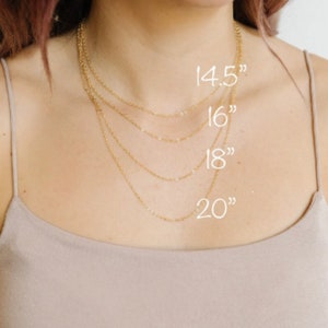 May include: A collection of delicate gold necklaces of varying lengths, displayed against a neutral background. The necklaces are 14.5, 16, 18, and 20 inches long, as indicated by the white text overlay. The chains are fine and elegant, suitable for layering.