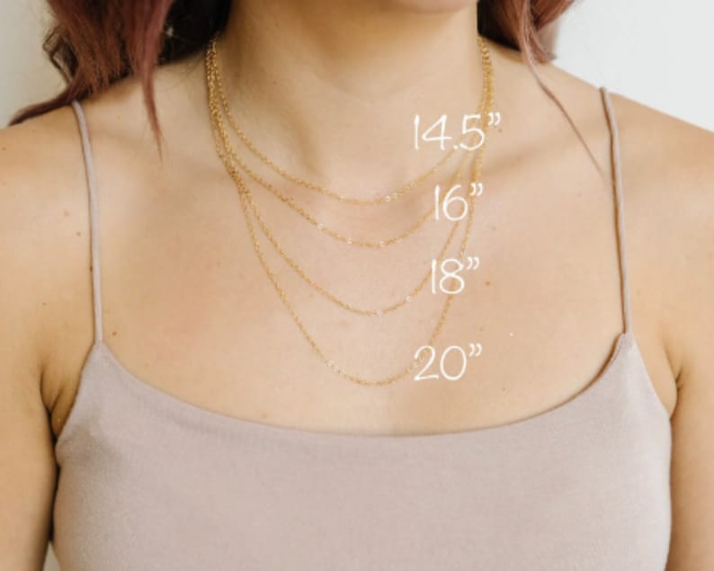 May include: A collection of delicate gold necklaces of varying lengths, displayed against a neutral background. The necklaces are 14.5, 16, 18, and 20 inches long, as indicated by the white text overlay. The chains are fine and elegant, suitable for layering.