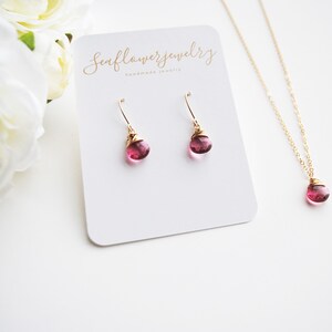 Puede incluir: Un conjunto de collar y pendientes dorados con un peque&ntilde;o colgante redondo de piedra rosa y pendientes a juego. Las joyas se exhiben en una tarjeta blanca con el texto "Seaflowerjewelry handmade jewelry".