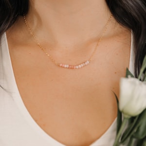 May include: A delicate gold chain necklace with a row of small pink and white beads.