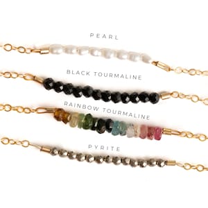 May include: Four strands of beads on gold chains, each with a different type of bead: pearl, black tourmaline, rainbow tourmaline, and pyrite.