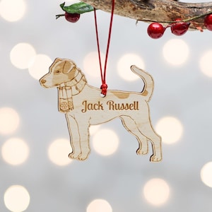 Könnte beinhalten: Weihnachtsbaumschmuck aus Holz in Form eines Jack Russell Terriers mit Schal. Der Anhänger hängt an einer roten Schnur und trägt die Worte "Jack Russell" eingraviert.