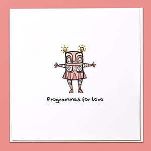 Könnte beinhalten: Eine Grußkarte mit einer rosa Roboterillustration. Der Roboter hat einen quadratischen Kopf, ausgestreckte Arme und einen Rock mit Herzdetails. Der Text "Programmed for love" steht darunter auf weißem Hintergrund.