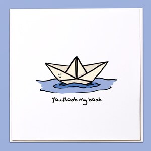 Puede incluir: Tarjeta blanca con un dibujo de un barco de papel sobre agua azul. El barco tiene una cara sonriente. Las palabras "You float my boat" están escritas en negro debajo, un diseño lindo y sencillo.