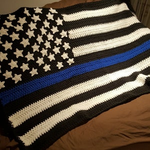 May include: A crocheted blanket in the style of the American flag with a blue stripe across the middle. The blanket is made with black, white, and blue yarn.