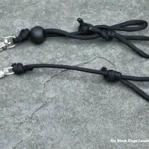 May include: Two black paracord leashes with silver swivel clips and a black bead. The leashes are knotted at the ends and have a loop at the top.