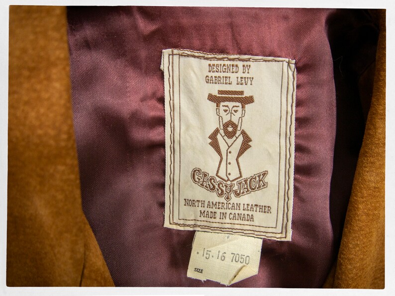 May include: A brown leather jacket with a burgundy lining and a label that reads "Designed by Gabriel Levy Gassy Jack North American Leather Made in Canada 15-16 7050 Size".