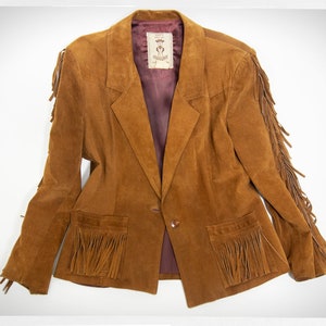 May include: A brown suede jacket with fringe detailing on the sleeves, pockets, and hem. The jacket has a single button closure and a burgundy lining.