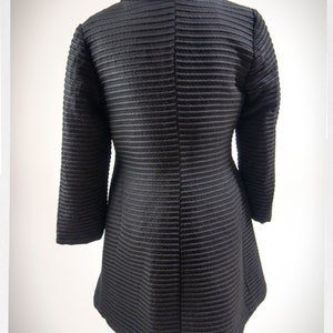 May include: A black, long-sleeved, collared jacket with a ribbed texture. The jacket has a high collar and a fitted silhouette.