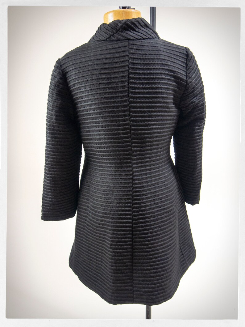 May include: A black, long-sleeved, collared jacket with a ribbed texture. The jacket has a high collar and a fitted silhouette.
