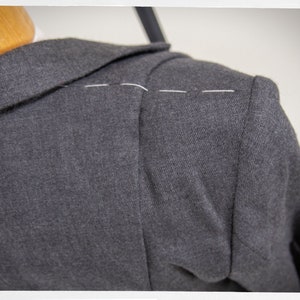 May include: Close-up of a dark gray blazer with a white thread seam along the shoulder.