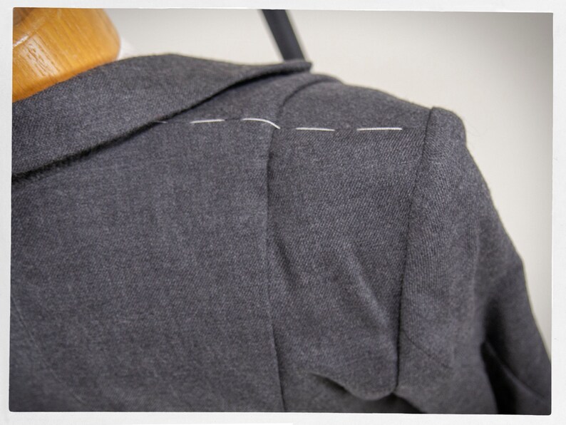 May include: Close-up of a dark gray blazer with a white thread seam along the shoulder.