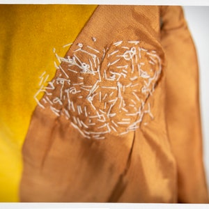 May include: Close-up of a brown fabric with a white stitched design. The fabric is folded over a yellow fabric.