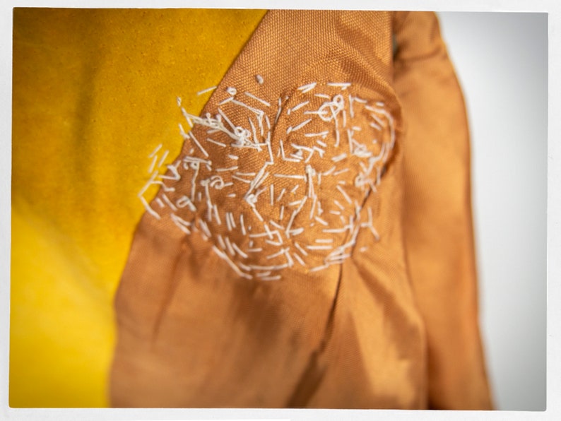 May include: Close-up of a brown fabric with a white stitched design. The fabric is folded over a yellow fabric.