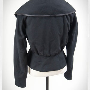 May include: Black fitted jacket with a wide, folded collar and a satin trim. The jacket has long sleeves and a fitted waist.