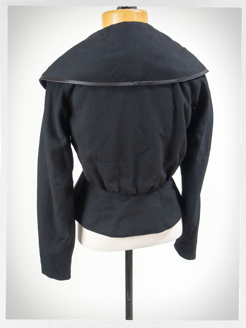 May include: Black fitted jacket with a wide, folded collar and a satin trim. The jacket has long sleeves and a fitted waist.
