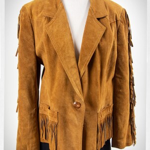 May include: A brown suede jacket with fringe detailing on the sleeves, hem, and pockets. The jacket has a single button closure and a classic blazer style.