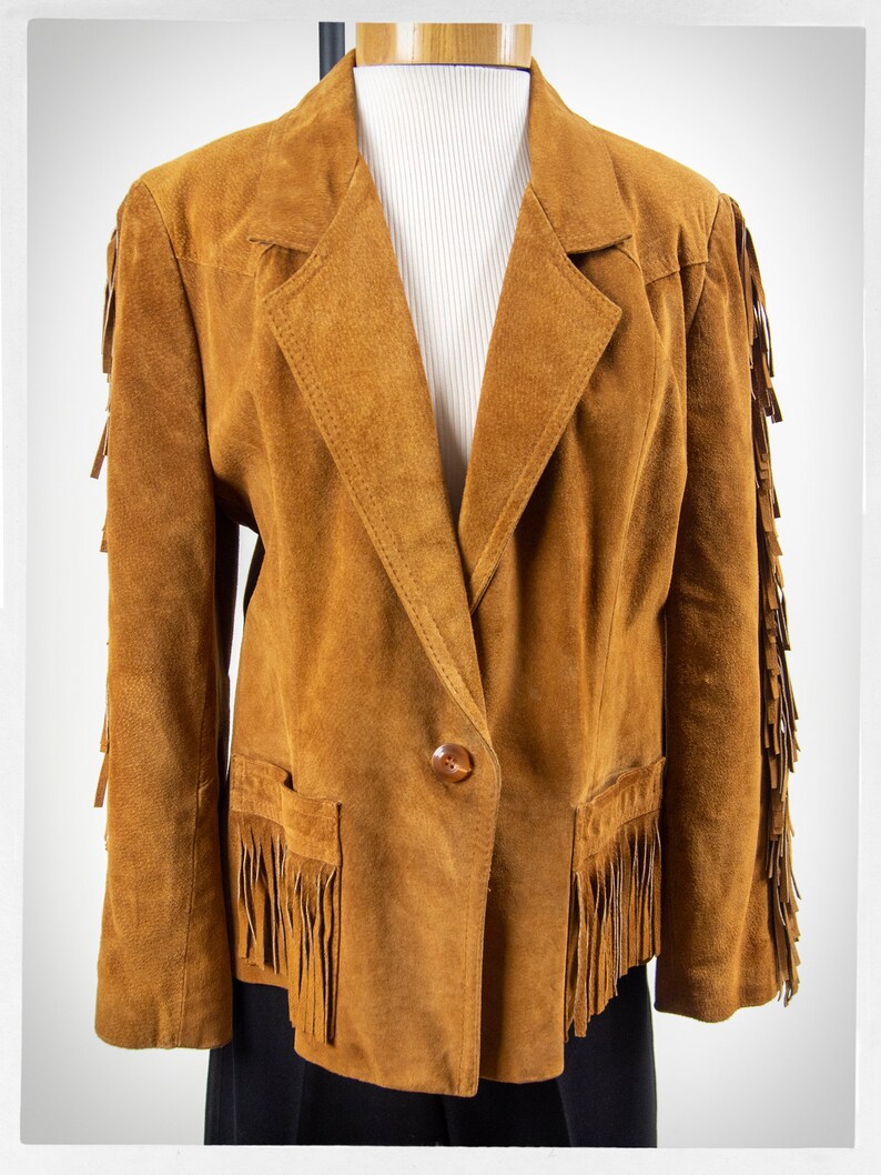 May include: A brown suede jacket with fringe detailing on the sleeves, hem, and pockets. The jacket has a single button closure and a classic blazer style.