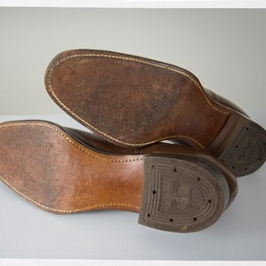 May include: Close-up of the brown leather soles of a pair of shoes. The soles are stitched and have a worn look.