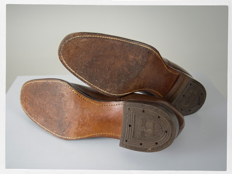 May include: Close-up of the brown leather soles of a pair of shoes. The soles are stitched and have a worn look.