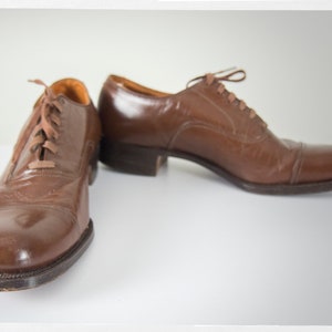 May include: A pair of brown leather lace-up shoes with a polished finish. The shoes have a closed toe and a low heel.