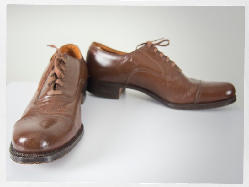 May include: A pair of brown leather lace-up shoes with a polished finish. The shoes have a closed toe and a low heel.