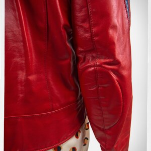 May include: A red leather jacket with blue and white stripes on the sleeves. The jacket has a zipper closure and a stand-up collar.