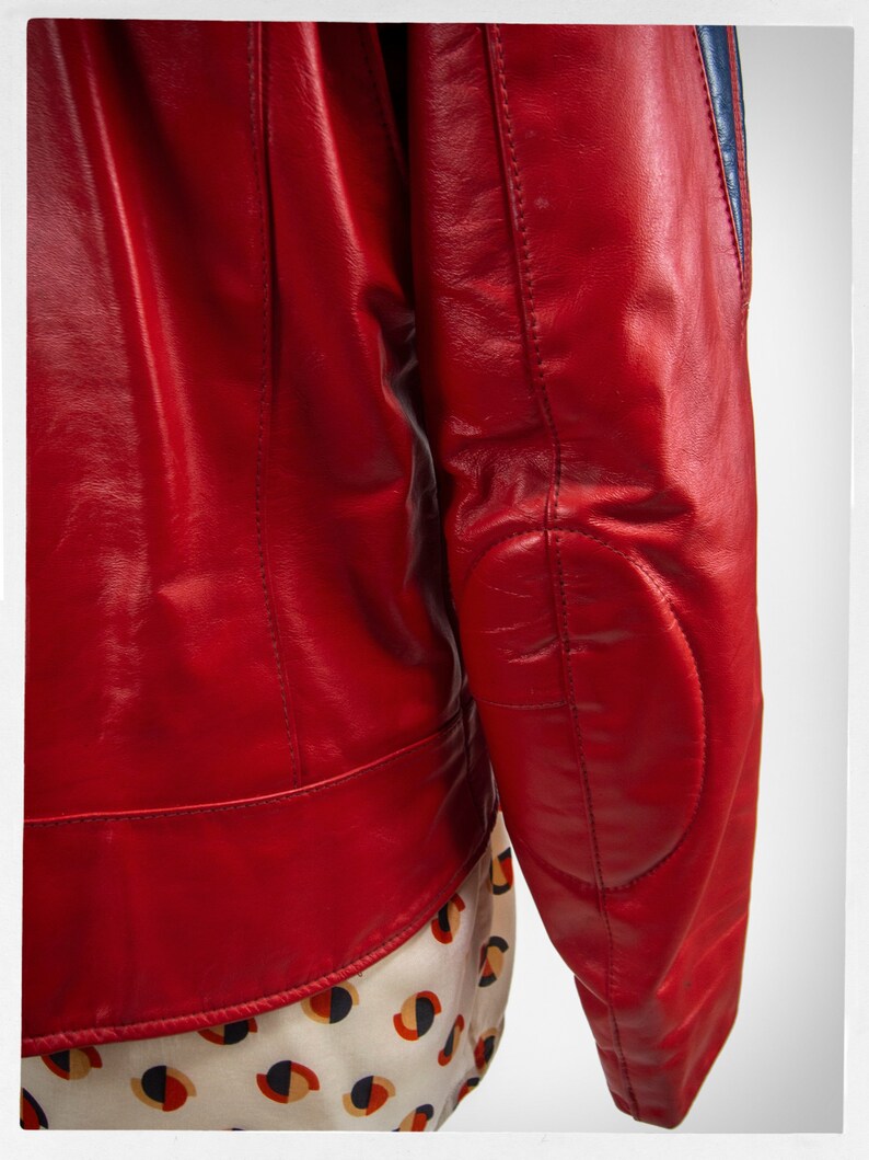 May include: A red leather jacket with blue and white stripes on the sleeves. The jacket has a zipper closure and a stand-up collar.