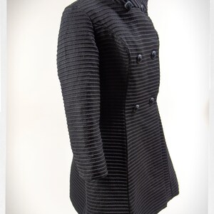 May include: A black, double-breasted coat with a high collar and a ribbed texture.