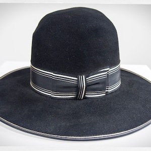 May include: A black felt hat with a wide brim and a black and white ribbon around the crown.