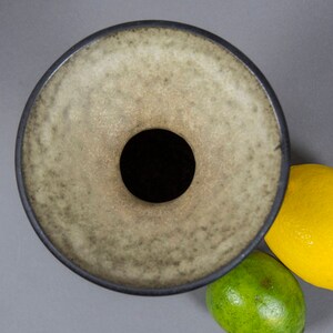 Peut inclure: Un vase en c&eacute;ramique avec une large ouverture ronde et un bord gris fonc&eacute;. Le vase a un gla&ccedil;age gris clair mouchet&eacute;.