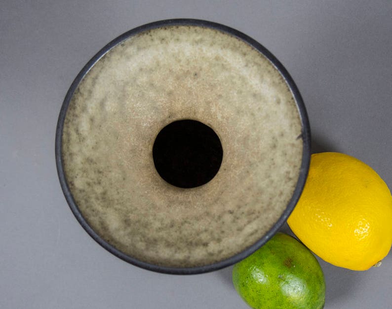 Peut inclure: Un vase en c&eacute;ramique avec une large ouverture ronde et un bord gris fonc&eacute;. Le vase a un gla&ccedil;age gris clair mouchet&eacute;.