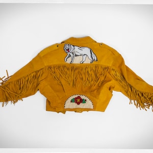 May include: A yellow suede jacket with fringe detailing and an embroidered wolf design on the back. The jacket also features a beaded flower design on the back.