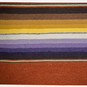 May include: A colorful woven rug with stripes of brown, yellow, purple, and red. The rug has a traditional design and is made of natural fibers.