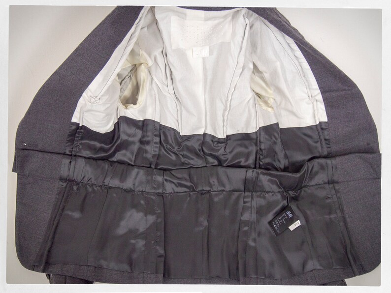 May include: The inside of a gray blazer with a black satin lining. The blazer has a label that reads "H&M Divided".