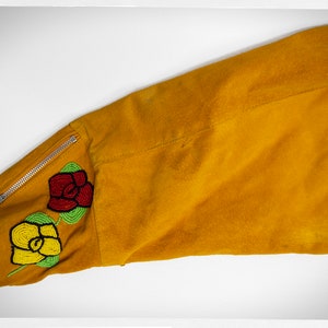 May include: A mustard yellow suede jacket with a zipper detail on the sleeve. The sleeve has a beaded design of two roses, one red and one yellow.